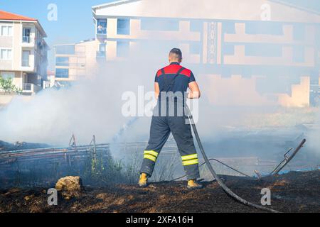 Feu dans le champ près de la ville. Pompier éteint un incendie. Banque D'Images