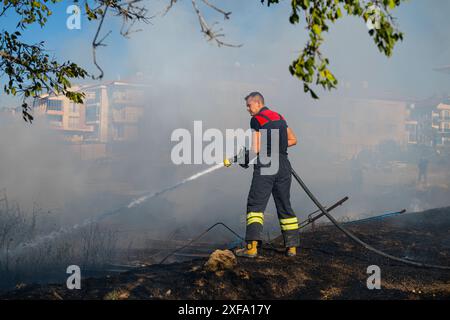 Feu dans le champ près de la ville. Pompier éteint un incendie. Banque D'Images