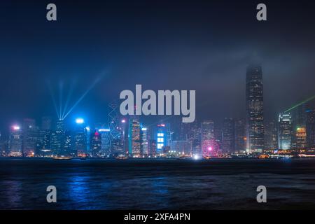 Magnifique paysage urbain nocturne de gratte-ciel d'affaires illuminé coloré avec spectacle d'éclairage laser sur le port Victoria en journée brumeuse à Hong Banque D'Images