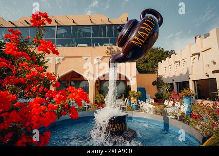 Un beau café en plein air avec une grande fontaine de théière et des fleurs rouges vibrantes. Banque D'Images