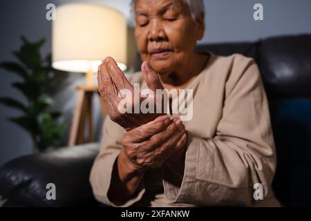 femme âgée souffrant de douleur au poignet tout en étant assise sur un canapé dans le salon la nuit Banque D'Images