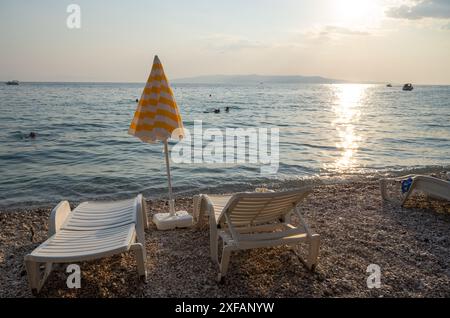 Makarska, Croatie. 1er octobre 2023. Un parasol rayé se tient entre deux chaises longues sur une plage. Crédit : Viola Lopes/dpa/Alamy Live News Banque D'Images