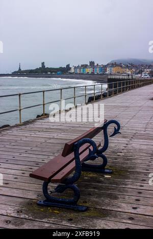 Décoratif en forme de serpent, bancs le long de la côte avec la ville d'Aberystwyth en arrière-plan sur une journée froide et brumeuse. Banque D'Images