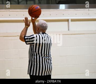 L'arbitre tourne un ballon de basket-ball sur le bout des doigts lors d'un match universitaire de lycée. Il porte un uniforme noir et blanc. Banque D'Images