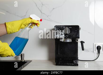 La jeune fille tient dans sa main un spray anti-graisse pour nettoyer la cuisine de la graisse et de la saleté. Lavage et nettoyage d'une machine à café et cuisine appli Banque D'Images