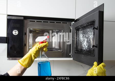 Spray anti-graisse dans la main d'une fille qui nettoie la cuisine. Nettoyer le four à micro-ondes de la graisse et de la saleté. Agent antistatique moderne. Banque D'Images