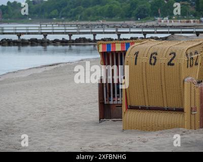 Chaise de plage jaune sur une plage de sable, vue sur l'eau et une jetée en bois en arrière-plan, Eckernfoerde, schlewsiwg-holstein, allemagne Banque D'Images