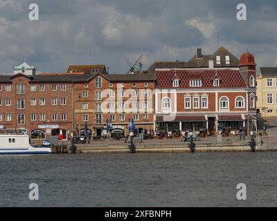 Bâtiments historiques le long du rivage avec terrasses de cafés et port au premier plan, ciel nuageux, Kappeln, schlewsig-holstein, allemagne Banque D'Images