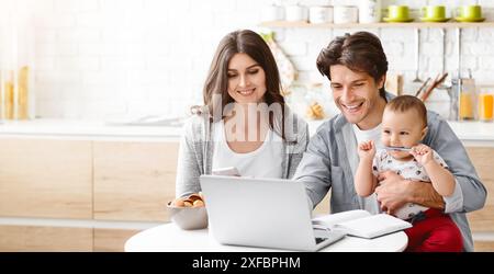 Famille heureuse travaillant à domicile avec bébé dans la cuisine Banque D'Images