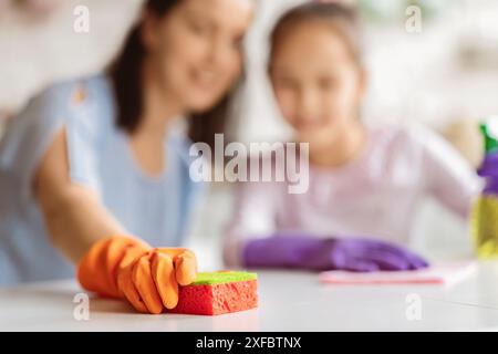 Femme tenant l'éponge de nettoyage pendant que sa fille nettoie dans la cuisine Banque D'Images