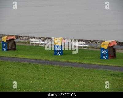 Trois chaises de plage colorées et bancs blancs sur une pelouse verte, atmosphère côtière calme sous un ciel nuageux, cuxhaven, allemagne Banque D'Images