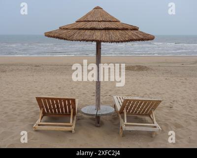 Deux chaises longues en bois vides sous un parasol sur une plage de sable tranquille par temps nuageux, Leyde, pays-Bas Banque D'Images