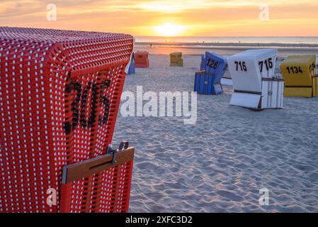 Chaise de plage numérotée rouge au premier plan, autres paniers et la mer en arrière-plan au coucher du soleil, langeoog, frise orientale, allemagne Banque D'Images