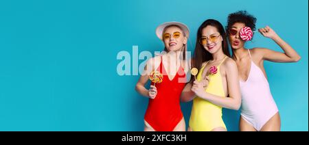 Trois jeunes femmes portant des maillots de bain et des lunettes de soleil tenant des sucettes Banque D'Images