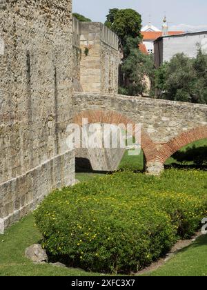 Un vieux mur de pierre avec un pont arqué rouge et un jardin bien entretenu avec des fleurs en fleurs entouré de bâtiments historiques, lisbonne, portugal Banque D'Images