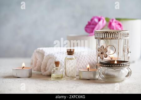 Bouteilles d'huile essentielle d'aromathérapie avec fleurs de rose de mai, bougies et accessoires de traitement spa sur fond blanc Banque D'Images