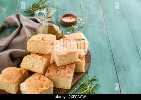 Focaccia. Recette traditionnelle italienne de pain et de pâtisserie coupée en morceaux pour servir avec de l'huile d'olive, des assaisonnements aromatiques et du romarin sur vieux rusti en bois Banque D'Images