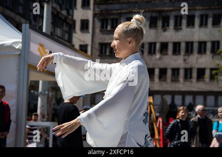 Un maître de Tai Chi serein dans un costume blanc fluide se produit gracieusement dans une rue animée, ses mouvements fluides contrastant avec la toile de fond urbaine vibrante Banque D'Images