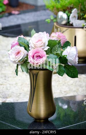 un vase en laiton élancé avec un bouquet artificiel de roses sur une tombe en marbre dans un cimetière Banque D'Images