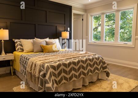Chambre à l'éclairage lumineux - grand lit avec couette à motifs géométriques et touches jaunes - tables de nuit avec lampes - vue sur la verdure par la fenêtre. Prise en charge dans Banque D'Images