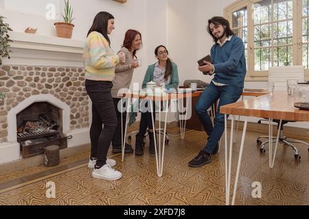 Un groupe de quatre collègues profite d'une réunion détendue, partageant des idées et discutant du travail dans un cadre de bureau confortable avec une cheminée. Banque D'Images