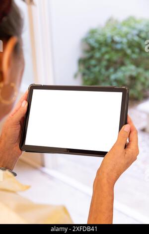 Tenant la tablette, femme regardant l'écran blanc près de la fenêtre à la maison, espace de copie Banque D'Images