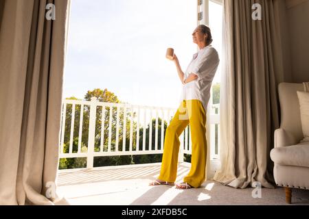 Debout par des portes ouvertes, femme senior profitant du café du matin à la maison, espace de copie Banque D'Images
