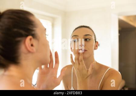 Application du baume à lèvres, jeune femme regardant dans le miroir à la maison Banque D'Images