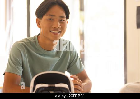 Garçon adolescent souriant assis au bureau avec casque VR dans la salle de classe du lycée Banque D'Images