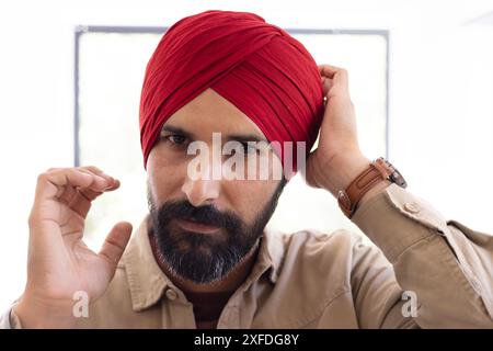 Ajustant turban rouge, homme avec la barbe regardant avec confiance la caméra à l'intérieur Banque D'Images