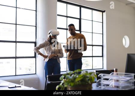 En utilisant un casque VR, femme collaborant avec un collègue examinant la tablette au bureau Banque D'Images