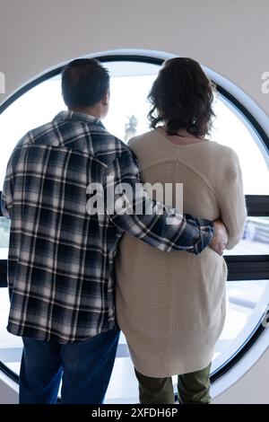 Couple senior debout ensemble, regardant autour de la fenêtre, serrant l'un l'autre Banque D'Images