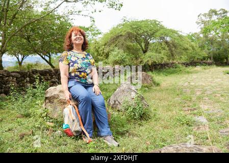 Femme hispanique mature souriant assis au repos lors d'une promenade sur un sentier historique rural, une voie royale en pierre restaurée, allant de Barichara à Guane, à San Banque D'Images