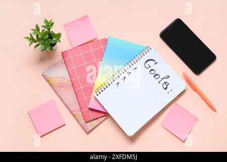 Liste des objectifs, carnets, notes adhésives et téléphone portable sur fond rose Banque D'Images