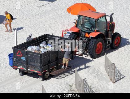 Les ouvriers municipaux vident les déchets des boîtes dans une remorque tractée par un tracteur sur une plage de sable Banque D'Images