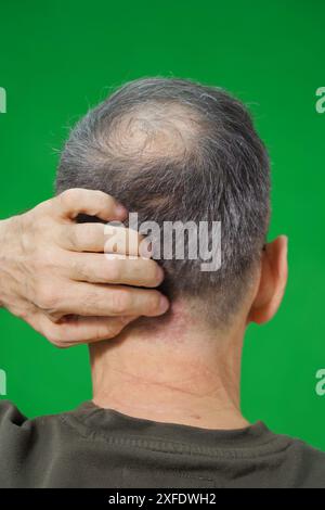 Un homme aux cheveux fins se tient debout dos au spectateur, sur fond vert Banque D'Images