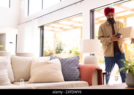 Transport boîte en carton, homme utilisant smartphone tout en marchant dans le salon, espace de copie Banque D'Images