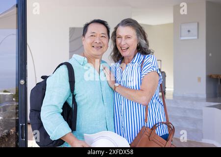 Couple senior souriant posant avec des sacs à dos et des chapeaux, prêt pour les vacances Banque D'Images