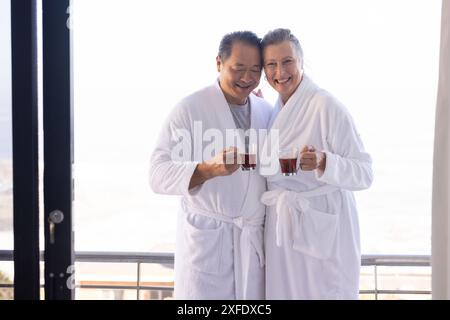 Couple senior dans des peignoirs appréciant le thé sur le balcon, souriant et relaxant Banque D'Images