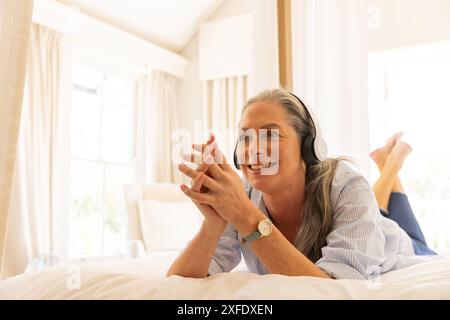 Écouter de la musique, femme mature se relaxant sur le lit avec des écouteurs, souriant Banque D'Images