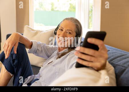 Écouter de la musique avec des écouteurs, femme mature souriant et tenant un smartphone Banque D'Images