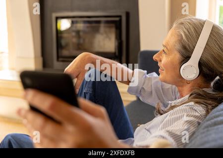 Écouter de la musique avec des écouteurs, femme mature se relaxant et tenant un smartphone Banque D'Images