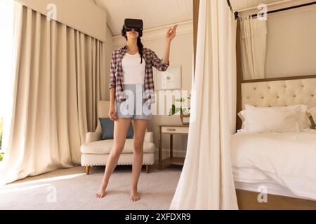 En utilisant un casque VR, femme debout dans la chambre et pointant vers quelque chose Banque D'Images