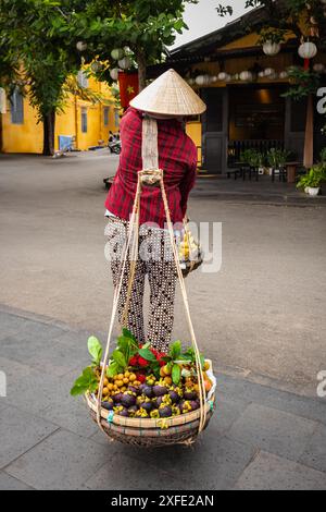 Femme vietnamienne portant des paniers de fruits. Une vendeuse locale vend des fruits qu'elle porte dans des paniers dans une vieille ville de Hoi an, au Vietnam. Str. Vietnamienne Banque D'Images