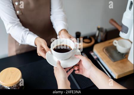 Gros plan d'une barista qui remet une tasse de café sur un comptoir à un client, travaillant dans un café. service, petite entreprise, temps partiel j Banque D'Images