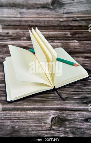 Ouvrez le carnet avec des pages vierges et un crayon vert sur une table en bois. Banque D'Images