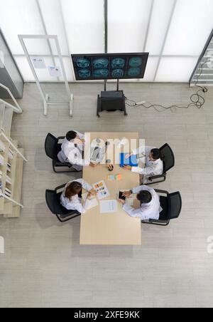 Groupe de professionnels de la santé engagés dans une discussion ou une réunion dans un cabinet médical. Un grand moniteur affichant plusieurs acquisitions cérébrales IRM, à tourner Banque D'Images