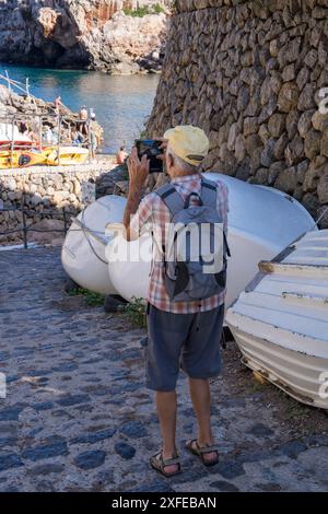 Un homme âgé parcourt le monde en utilisant son téléphone pour photographier le paysage urbain du petit village côtier de Deia à Majorque, en Espagne. Hous traditionnel Banque D'Images