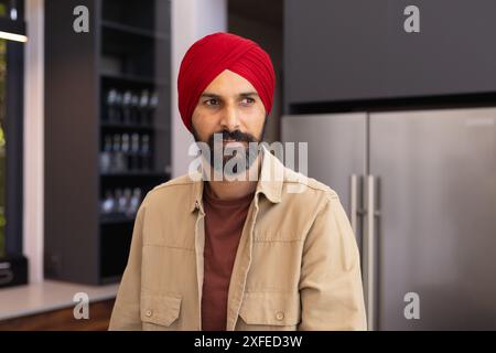 Homme en turban rouge debout dans la cuisine moderne, regardant réfléchi Banque D'Images