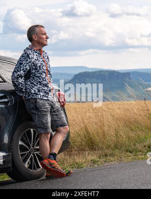 Un homme d'âge moyen voyage en voiture autour de Meath. Il se tient près de la voiture et regarde le paysage montagneux. Suisse saxonne, Allemagne Banque D'Images